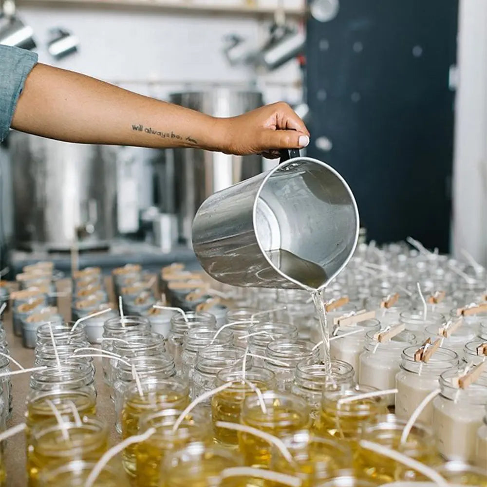 Person pouring liquid wax into candle jars in a studio setting