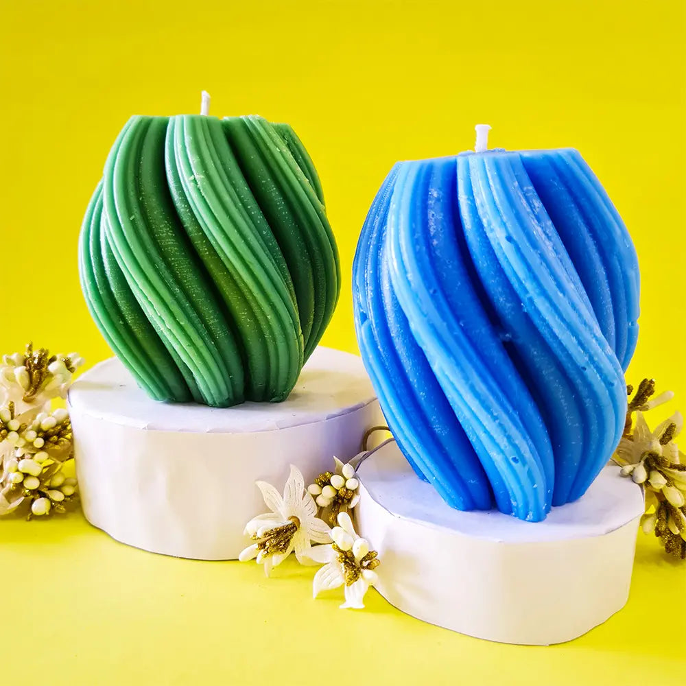 Two green and blue spiral swirl wave scented pillar candles on white podiums with a yellow background